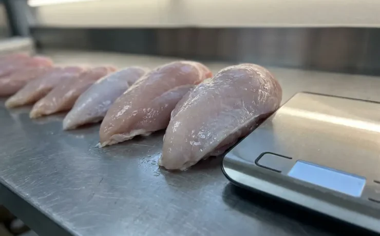 Frische Putenbrust-Filets nach Größe sortiert auf Edelstahl-Fleischertheke mit Küchenwaage, Nahaufnahme.